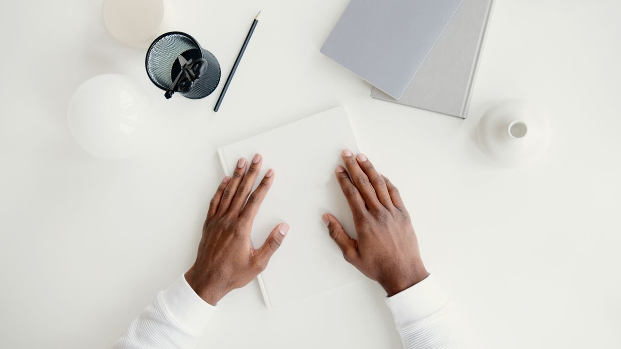 A pair of hands on a minimalist white desk with stationery and books, ideal for business or office concepts.